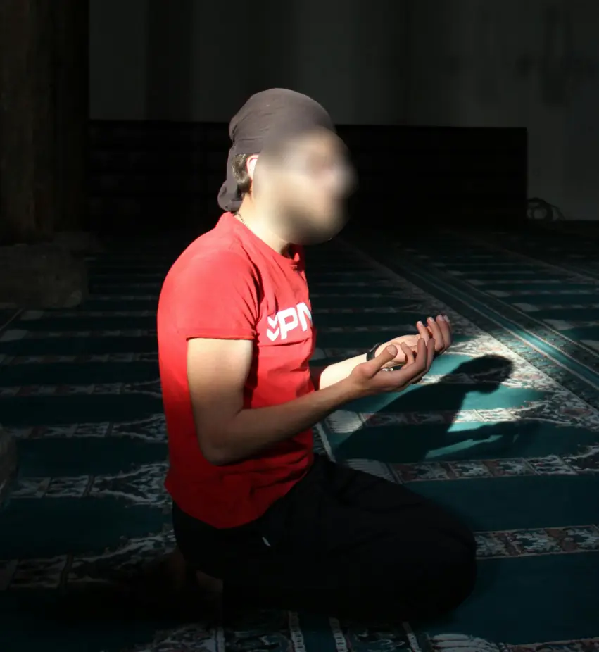 Muslim man in a prayer position with raised hands, in a calm setting dedicated to reflection and supplication.