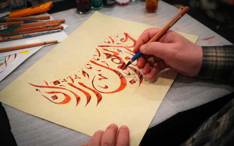Arabic calligraphy being drawn with a brush on paper