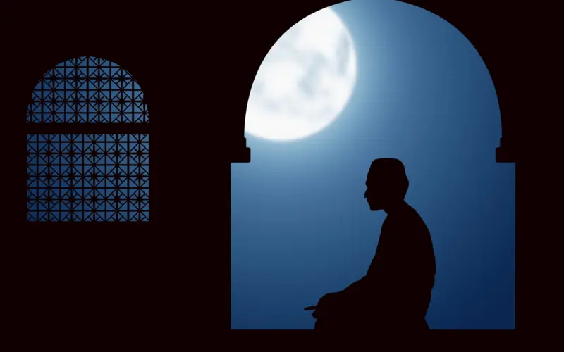 Silhouette of a man praying at night under the moon