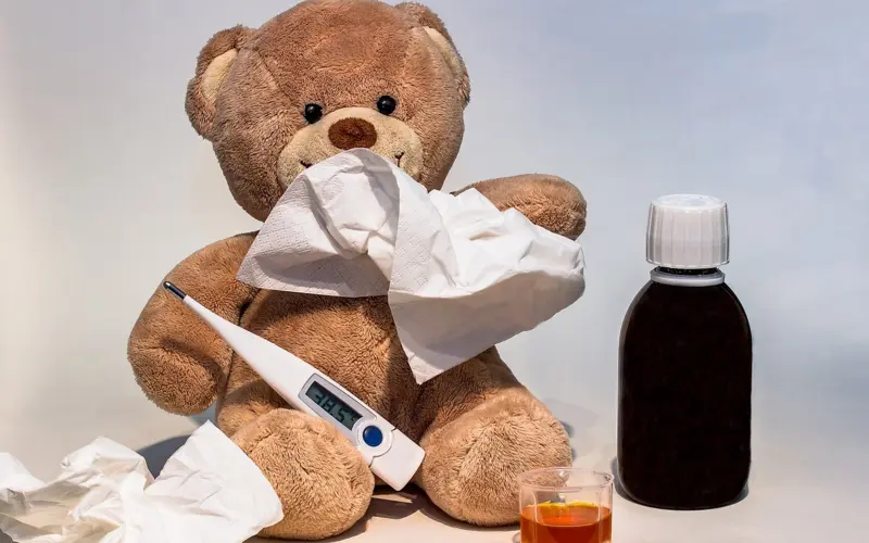 Sick teddy bear with thermometer and syrup