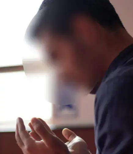 Man praying with raised hands near a window, bathed in natural light, expressing serenity and spiritual reflection.