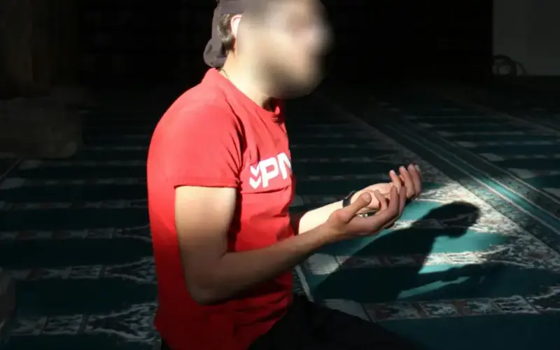 Muslim man in a prayer position with raised hands, in a calm setting dedicated to reflection and supplication.