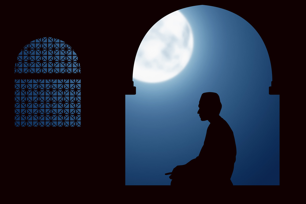 Silhouette of a man praying at night under the moon
